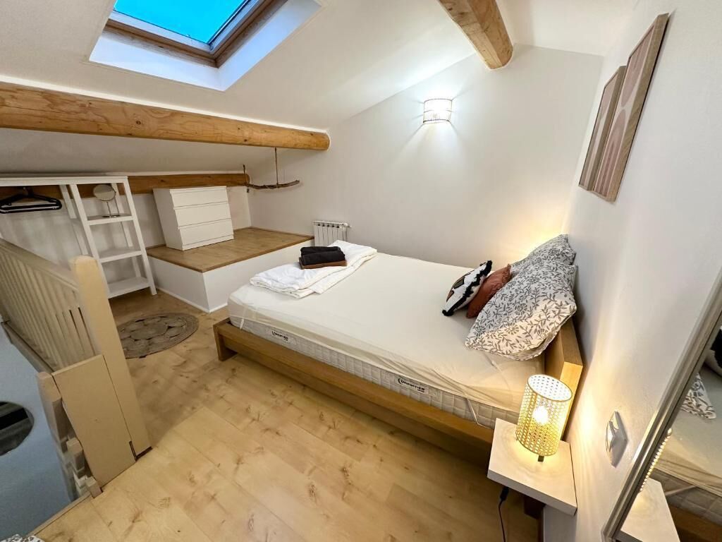 A compact bedroom with a loft bed, built-in storage, a skylight, and a bedside lamp.