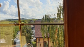Une fenêtre donnant sur un bâtiment avec un toit recouvert de tuiles et un arbre devant.