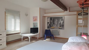 Une chambre à coucher avec un lit, un bureau avec un ordinateur, une chaise, un radiateur et une fenêtre avec des stores.