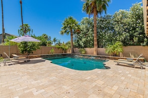 A swimming pool with a tiled deck, surrounded by palm trees and a brick wall.