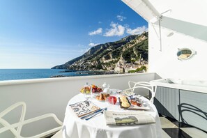 A table set with breakfast items and a newspaper on a balcony overlooking a coastal town. - Palazzo Don Salvatore (Amalfi)