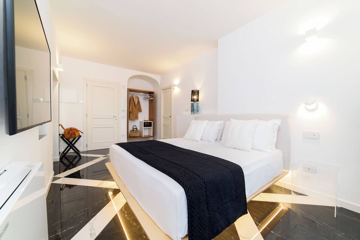 Une chambre d’hôtel moderne avec un grand lit, un miroir, une armoire et une salle de bain visible à travers une arche.