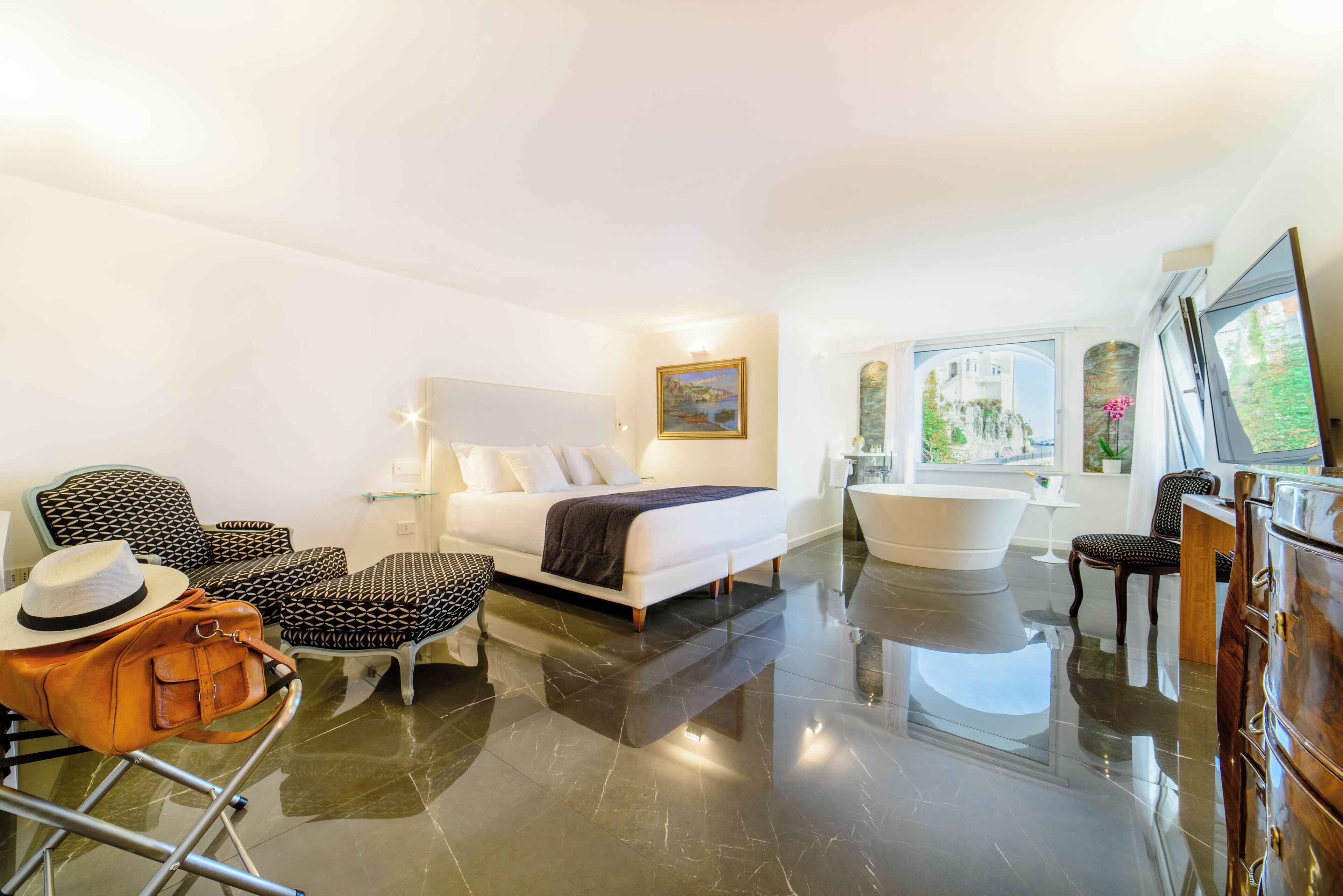 Una habitación de hotel moderna con una cama grande, una zona de estar con sillones estampados, un tocador con espejo y una bañera.