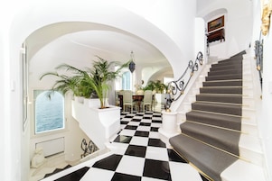 Una imponente escalera con piso a cuadros que conduce a un comedor con vistas al mar.