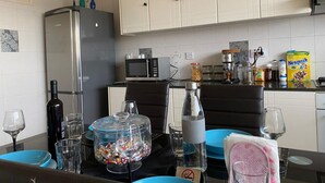 A modern kitchen with white cabinets, a refrigerator, a microwave, and a coffee machine. There are various kitchen items on the counter, including a bottle, a glass, and a box of cereal. - Larnaca Comfort Rooms (Larnaca)