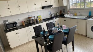 A kitchen with white cabinets, a black countertop, and a dining table set for four. - Larnaca Comfort Rooms (Larnaca)