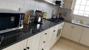 A kitchen with white cabinets, a black countertop, a microwave, a stove, and a window. - Larnaca Comfort Rooms (Larnaca)