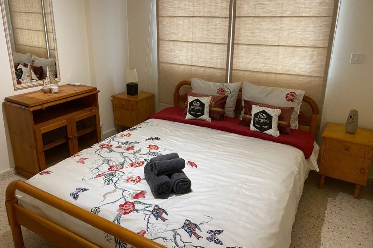 Ein ordentlich eingerichtetes Schlafzimmer mit einem Bett, einem Nachttisch aus Holz, einer Kommode und einem Spiegel.
