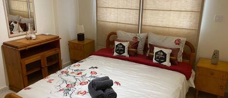 A neatly arranged bedroom with a bed, a wooden nightstand, a dresser, and a mirror.