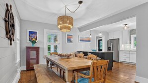 A spacious kitchen with a wooden dining table, chairs, and a hanging light fixture.