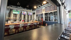 Un bar doté de tireuses à bière en acier inoxydable, d’un comptoir et de chaises rouges.