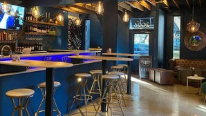 Un espace bar agrémenté de poutres en bois, de luminaires suspendus, d’un comptoir, de tabourets et d’une enseigne indiquant que le bar est ouvert.