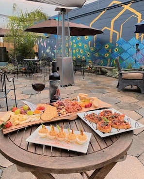 Un espace de restauration en plein air proposant une variété de plats et de boissons, notamment une bouteille de vin, une planche de charcuterie et des amuse-gueules.