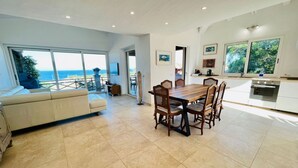 A spacious living area with a large dining table, a sofa, and a view of the ocean. - Villa a schiera Punta Aldia (Puntaldia)