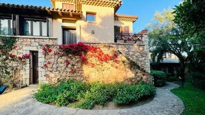 A stone house with a stone facade, a curved stone pathway, and lush green plants. - Villa a schiera Punta Aldia (Puntaldia)