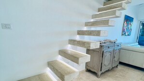 A modern staircase with built-in lighting, leading to a living area with a sofa and a cabinet. - Villa a schiera Punta Aldia (Puntaldia)