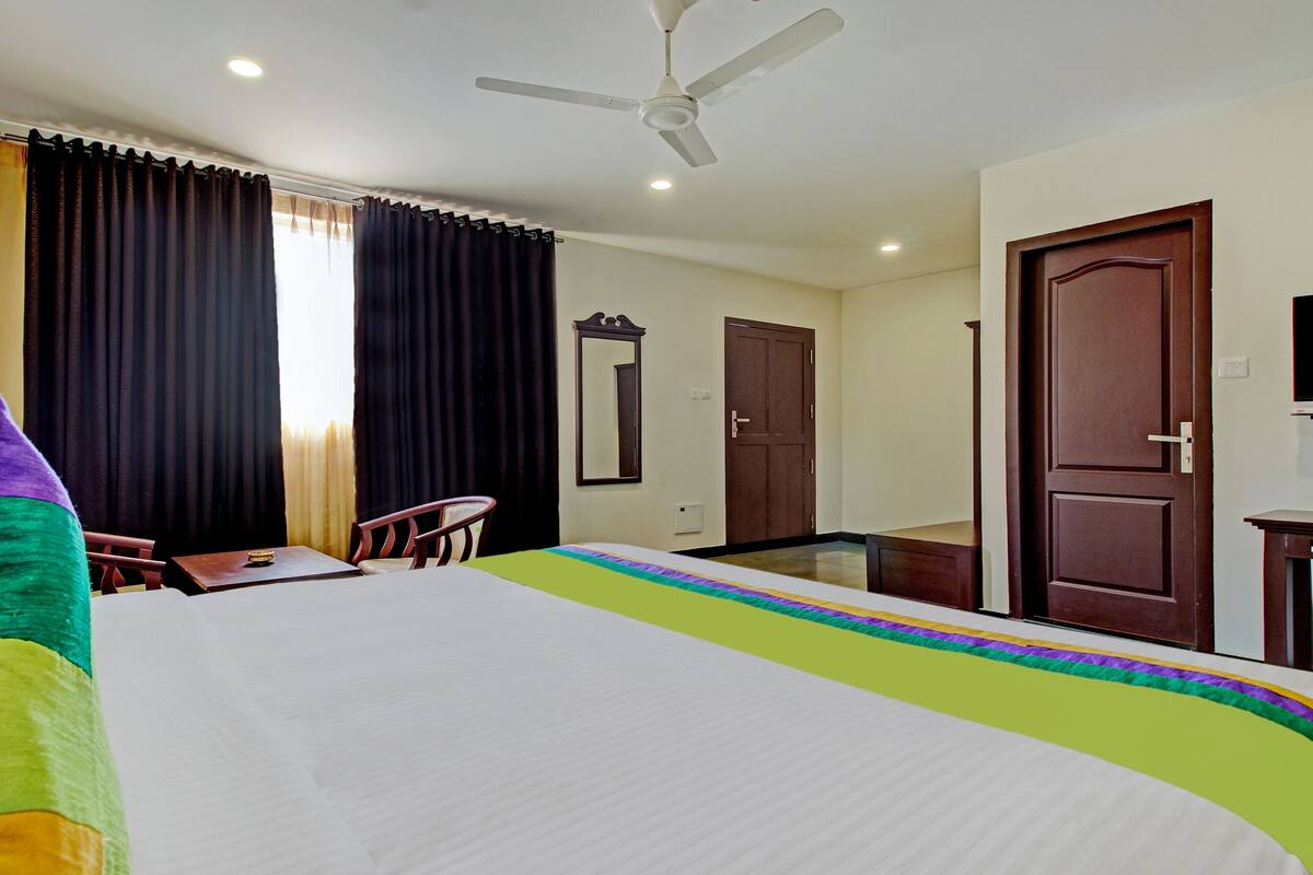 A hotel room with a bed, a desk, a chair, a ceiling fan, and a door.