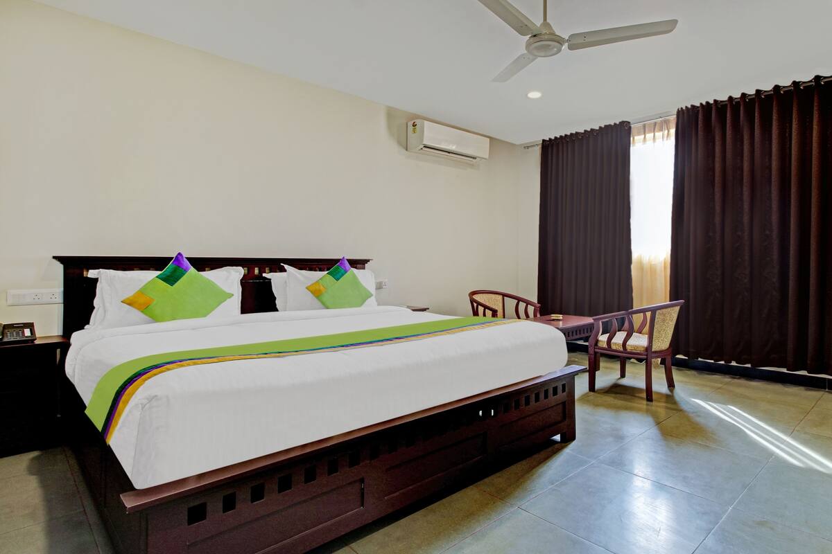 A hotel room with a bed, a desk, a chair, an air conditioner, and a window with curtains.