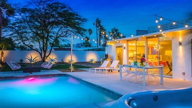 Een modern buitenzwembad met ligbedden en een jacuzzi, omringd door een verlicht terras met sfeerverlichting.