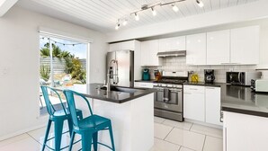 Een moderne keuken met witte kastjes, roestvrijstalen apparatuur en een centraal keukenblok met barkrukken.