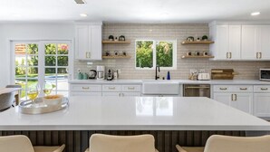 Une cuisine moderne avec des meubles blancs, un grand îlot central et une vue sur la verdure à l’extérieur.