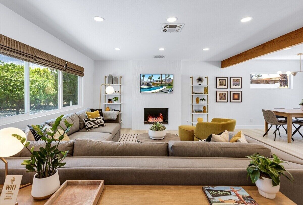 A modern living room with a large sofa, a fireplace, a TV, and a dining area.