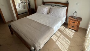 A bedroom with a bed, a wooden nightstand, a mirror, and a hanging light fixture. - Qta.da Flor - Fantastic Apartment With Pool (Albufeira)
