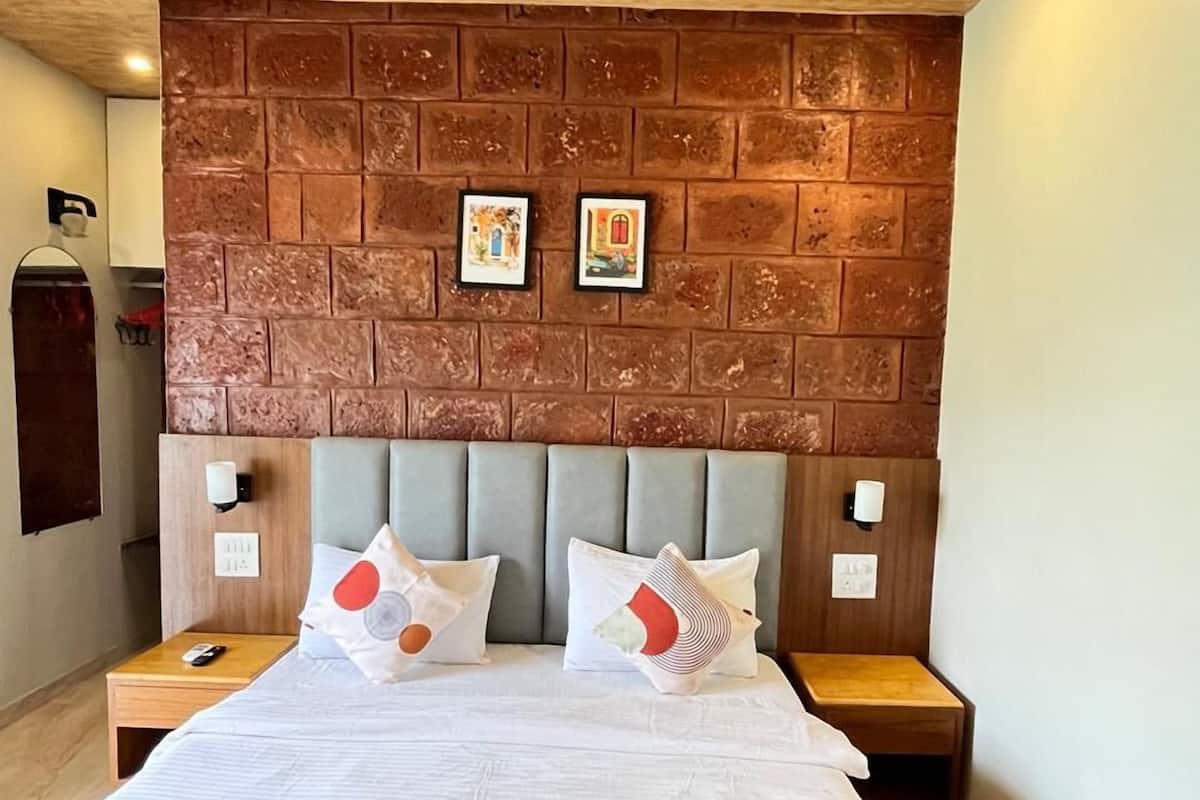 Habitación de hotel con cabecera de ladrillo, cama con ropa de cama blanca y detalles en rojo, dos mesitas de noche, un ventilador de techo y un equipo de aire acondicionado.