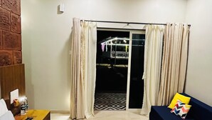 Hotellihuone, jossa on sänky, sohva, pieni pöytä, tiiliseinä, kattotuuletin ja liukuovi, joka johtaa ulkotilaan.