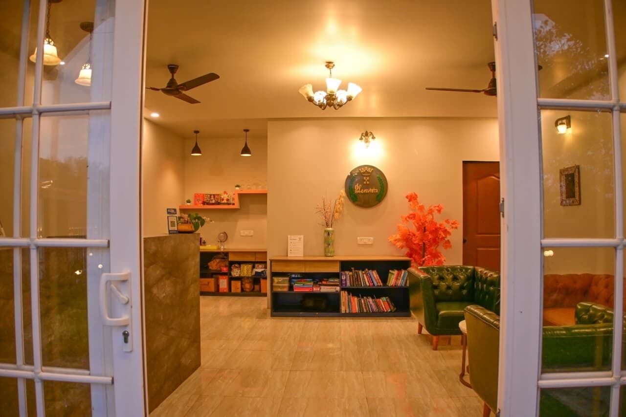 A reception area with a chandelier, ceiling fans, a bookshelf, and green leather sofas.