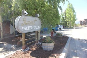 Placa do Summit Yacht Club, rodeada por árvores e área ajardinada com vasos.