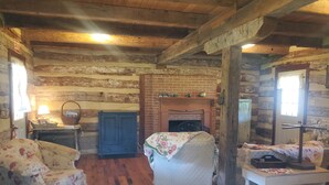 Interior rústico de una cabaña de troncos con chimenea, muebles de madera y techo de madera.