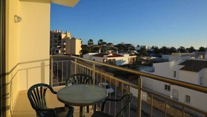A balcony with a table and chairs, overlooking a residential area with buildings and trees. - Magnolia - Beach & Pool - Fantastic T2 (Albufeira)