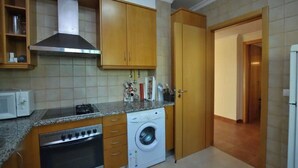A compact kitchen with wooden cabinets, a microwave, a stove, and a washing machine. - Magnolia - Beach & Pool - Fantastic T2 (Albufeira)