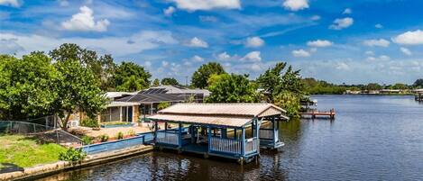 A waterfront property with a covered dock, a small building with a sloped roof, and a clear view of the water.