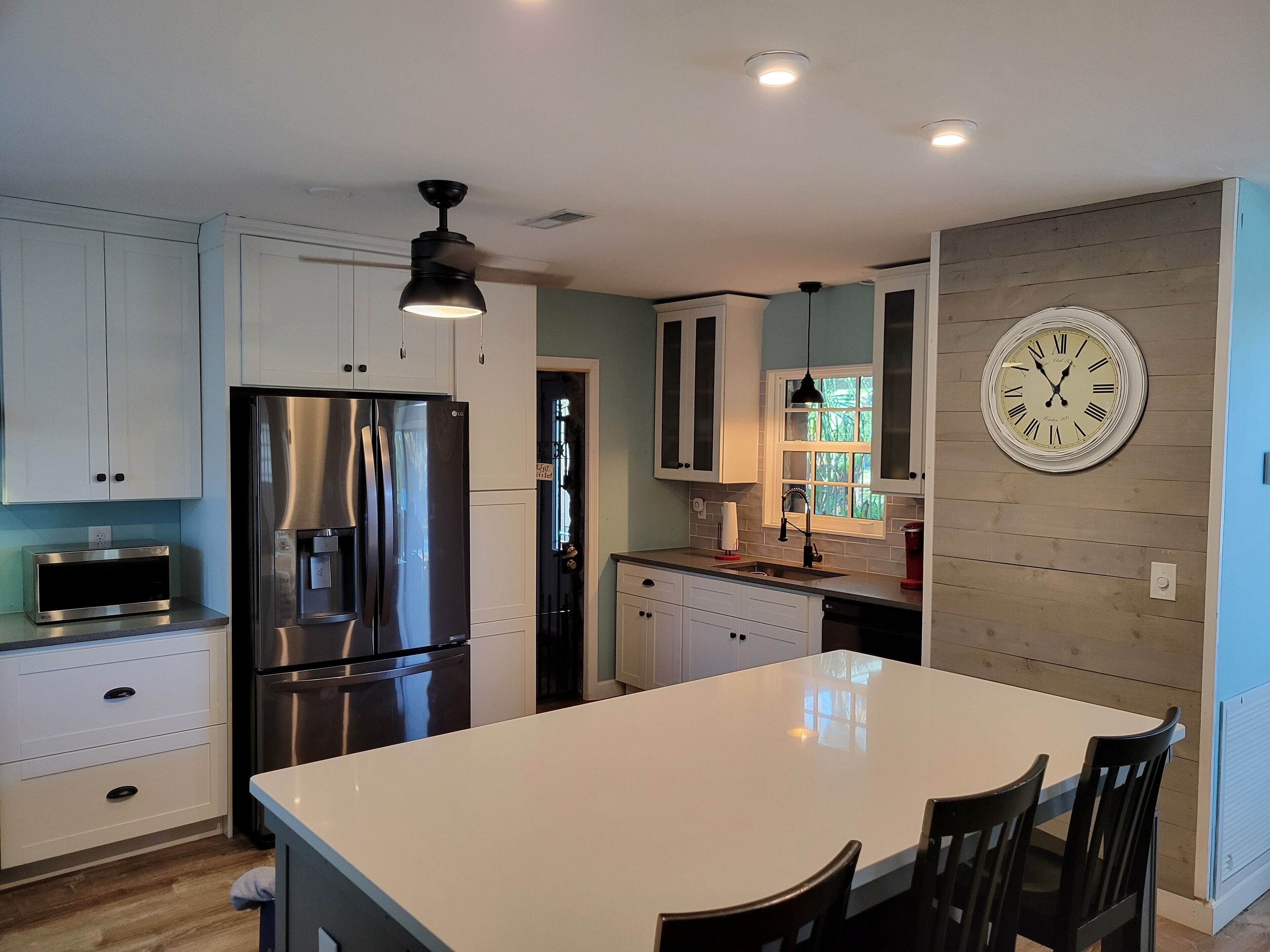 Una cocina moderna con armarios blancos, un refrigerador de acero inoxidable, una isla grande y un reloj de pared.
