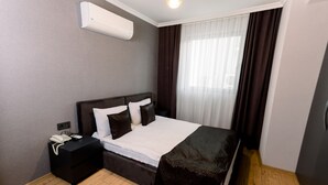 Ett modernt hotellrum med en stor säng, ett nattduksbord med en telefon och en luftkonditioneringsanläggning på väggen.