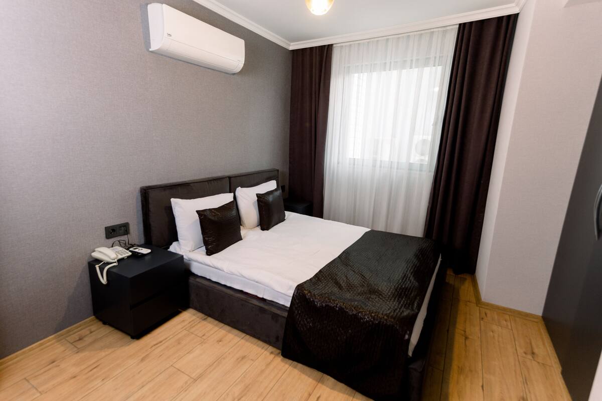 A modern hotel room with a large bed, a bedside table with a phone, and an air conditioning unit on the wall.