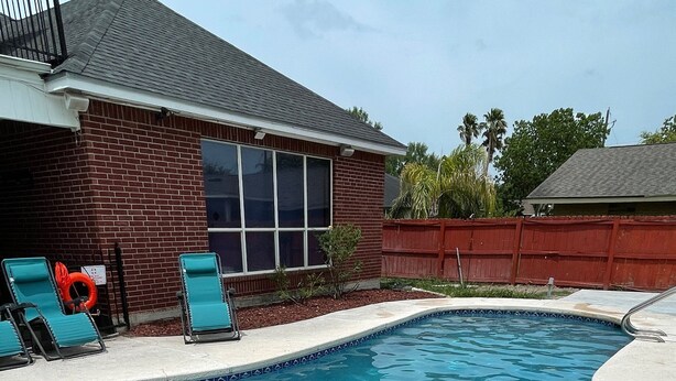 Une piscine à l’eau d’un bleu limpide, entourée d’une maison en briques et d’une clôture rouge.