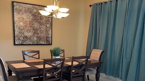 Un espace repas comprenant une table, des chaises, un lustre, un tableau et des rideaux.