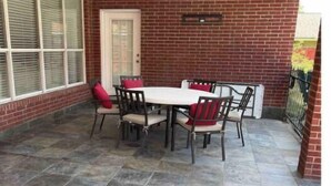 Un patio couvert avec un mur en briques, un ventilateur de plafond, une porte blanche et une table avec des chaises.