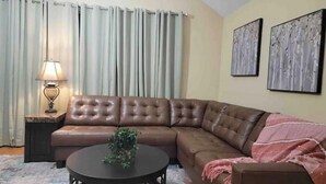 Un salon avec un canapé en cuir marron, une table basse ronde, une lampe et deux tableaux abstraits accrochés au mur.