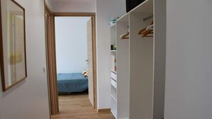 Un corridoio con pavimento in legno che conduce a una camera da letto con un letto e un armadio.