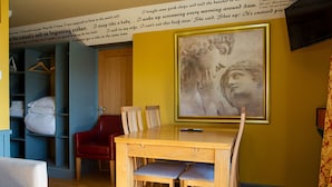 A room with a wooden dining table, two chairs, a red chair, a bed with white linens, a wardrobe, and a large framed artwork on the wall. - The Star Inn (Stroud)