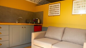 A compact kitchen with a grey cabinet, a red appliance, and a beige sofa in a room with yellow walls. - The Star Inn (Stroud)