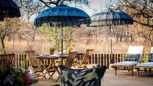 An outdoor deck with a wooden table, chairs, and umbrellas. - Safari Moon Luxury Bush Lodge (Hoedspruit)