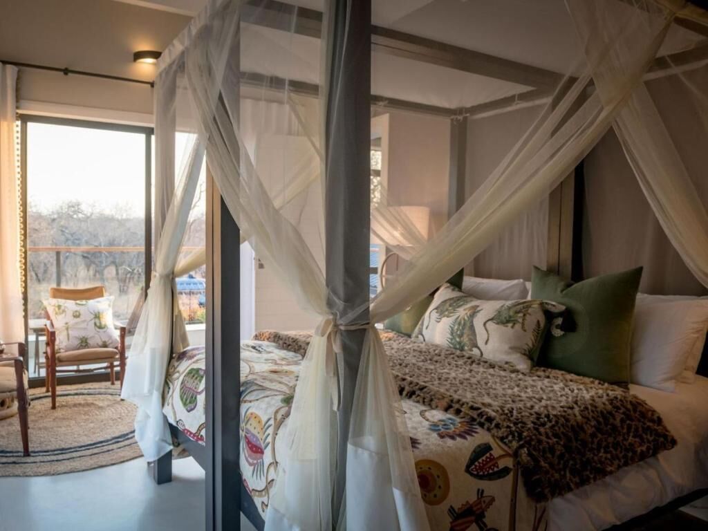 A bedroom with a four-poster bed, a view of the outdoors, and a chair by the window.