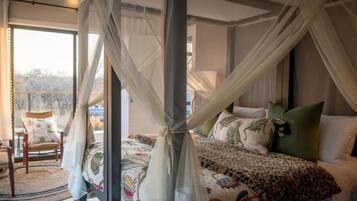 A bedroom with a four-poster bed, a view of the outdoors, and a chair by the window.