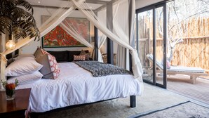 A bedroom with a canopy bed, a large painting, and a view of an outdoor deck. - Safari Moon Luxury Bush Lodge (Hoedspruit)