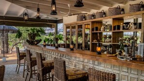 A bar area with wicker chairs, a wooden counter, and shelves with various items. - Safari Moon Luxury Bush Lodge (Hoedspruit)